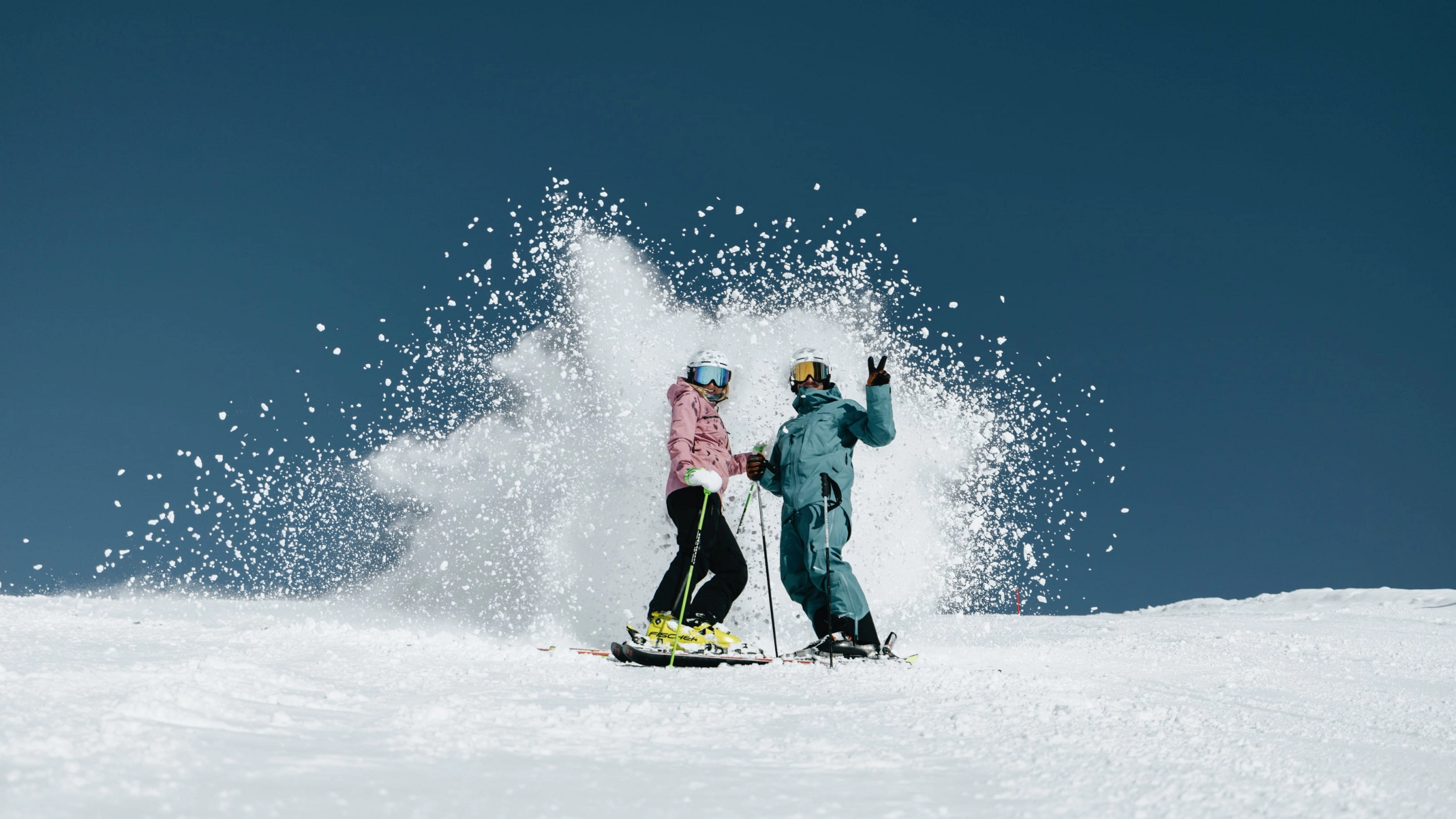 Zwei Skifahrer im Skigebiet Saalbach-Hinterglemm, Schnee spritzt auf.