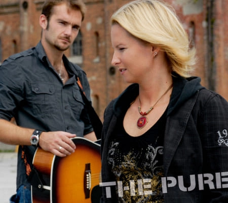 Zwei Musiker stehen draußen vor einer alten Fabrik.