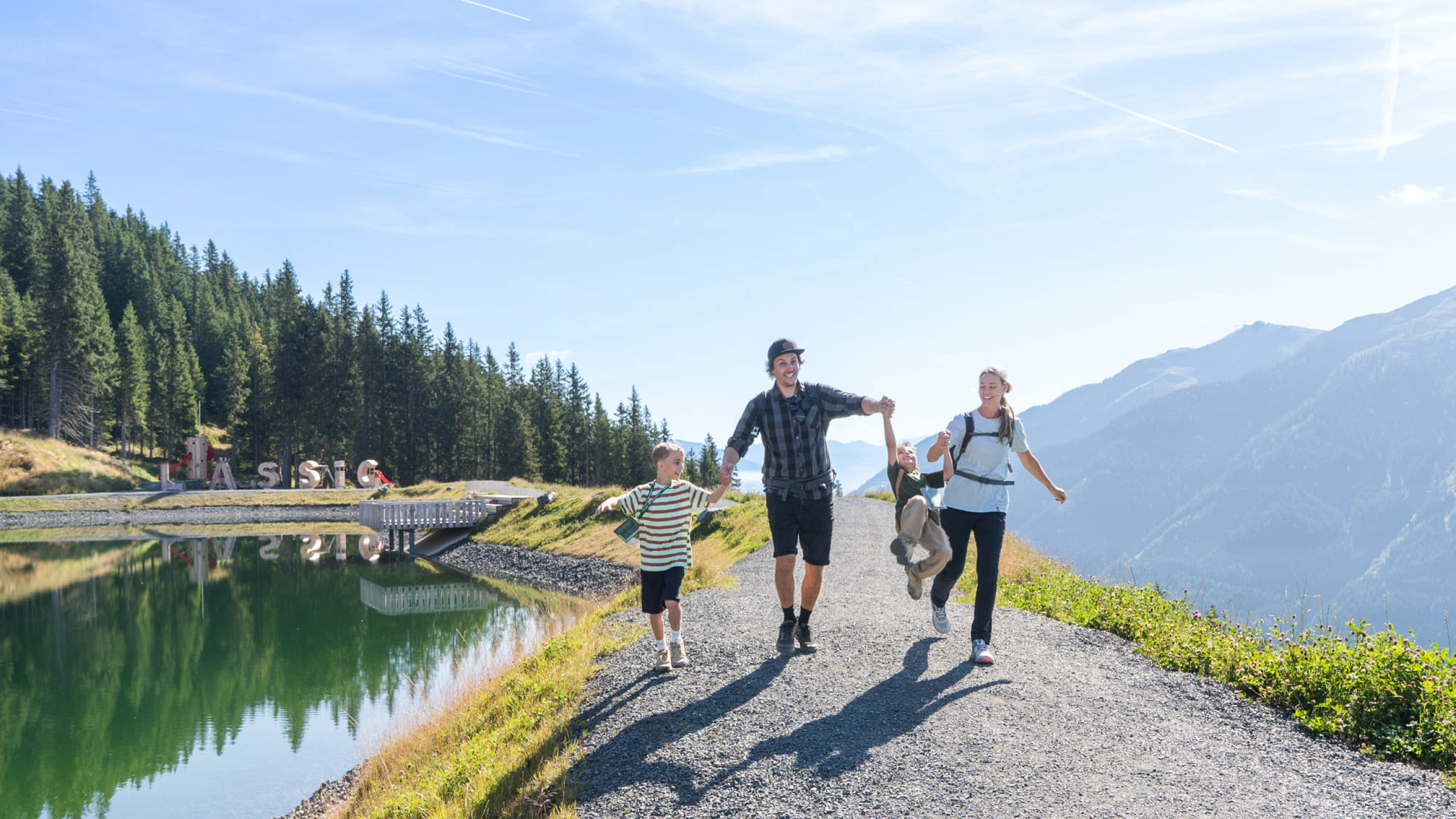 Familie wandert am Reiterkogel entlang eines Weges mit See.